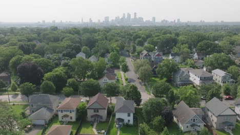 Drone-shot-of-beautiful-houses-with-greenery-and-famous-skyline-of-minneapolis-at-background-in-Minnesota,-USA