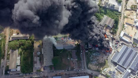 Dramatic-aerial-view-of-a-factory-engulfed-in-flames,-with-thick-black-smoke-rising-as-fierce-flames-consume-the-structure,-creating-total-chaos-and-destruction