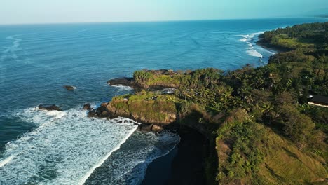 Craggy-rock-cradles-idyllic-Balianese-coastline,-incoming-tide,-aerial