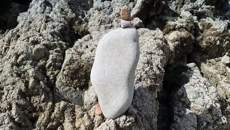 Balanced-zen-like-pebble-stone-tower-stacked-on-rugged-beach-rocks-at-sunrise