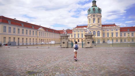 Junge-Frau-Genießt-Eine-Moderne,-Umweltfreundliche-Fahrt-Auf-Einem-Elektroroller-Zum-Historischen-Schloss-Charlottenburg-In-Berlin-Und-Verbindet-Tradition-Mit-Moderne