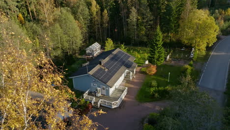 Drone-rising-over-a-foliage-branches,-toward-a-sustainable-home,-sunny,-fall-day