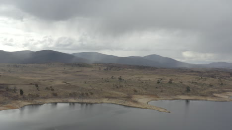 Drone-shot-of-the-shoreline-and-distant-mountains-around-Lake-Jindabyne-on-an-overcast-winters-day