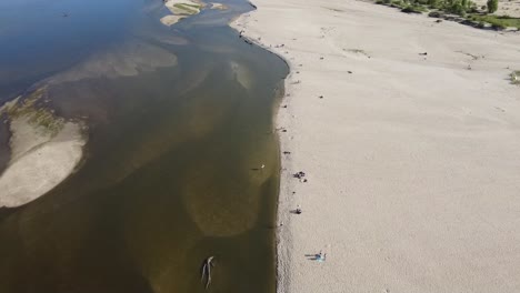 Aerial-view-of-sandy-riverbank,-with-people-on-the-beach-relaxing