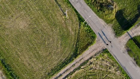 Two-cyclist-passing-a-grassy-desolate,-empty-crossroad