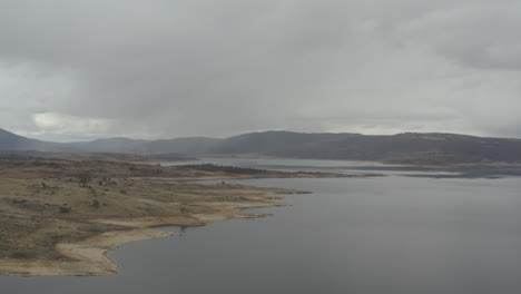 Drone-shot-of-the-shoreline-and-distant-mountains-around-Lake-Jindabyne-on-an-overcast-winters-day