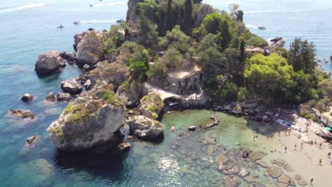 Drone-shot-of-Isola-Bella-in-Taormina,-with-people-relaxing-on-the-beach-shore