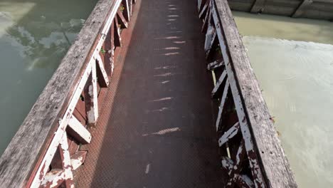 Couple-explores-across-metal-bridge-with-weathered-wooden-railings-over-river-in-Thailand