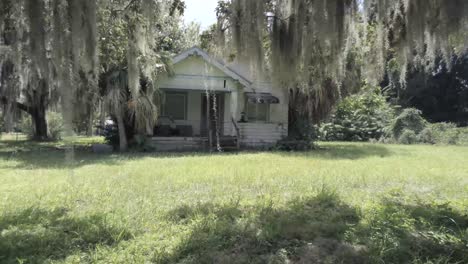 Abandon-house,-zoom-in-under-moss-filled-oak-trees-and-overgrown-yard