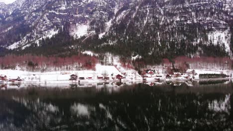 Aerial,-reverse,-drone-shot-away-from-buildings-on-the-snowy-coast-of-Lake-Fuschl,-cloudy-day,-in-Salzburg,-Austria