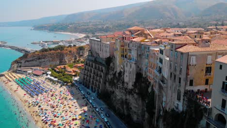 Luftaufnahme,-Drohnenaufnahme-Mit-Blick-Auf-Gebäude-Auf-Einem-Steilen-Hügel-Und-Den-Strand-Voller-Touristen,-Sonniger-Tag,-In-Tropea,-Vibo-Valentia,-Kalabrien,-Süditalien