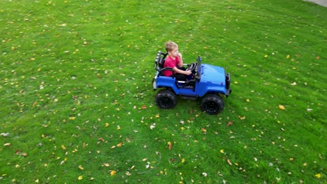 Ein-Kleines-Kind-Genießt-Eine-Fahrt-In-Einem-Blauen-Elektrischen-Spielzeugauto-Auf-Einem-Grünen-Rasen,-Der-Mit-Herbstblättern-übersät-Ist