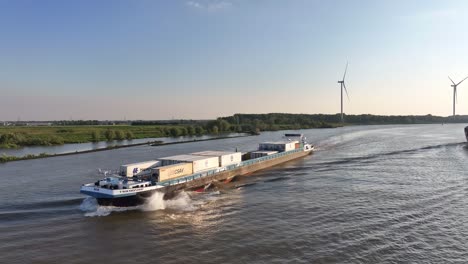 Two-ships-sail-on-a-wide-river-with-a-wind-turbine-in-the-background-on-a-clear-day