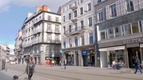 A-red-electric-tram-passes-by-the-camera-on-a-quiet-French-street-in-Clermont-Ferrand-with-buildings-in-the-background