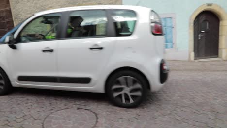 white-car-passing-through-a-narrow-street-in-Creux-Du-Van,-Neuchatel,-Switzerland-on-May-22,-2022