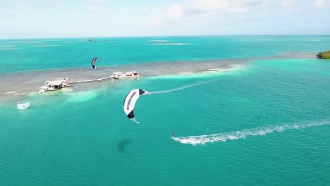 MEN-FLY-AND-JUMP-KITESURFING-PIRUETS,-AERIAL-SHOT-PALAFITO-LOS-ROQUES