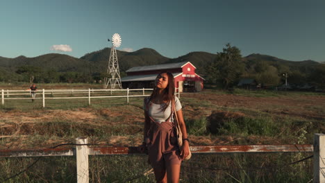 Attractive-girl-stay-by-fence-at-countryside-farm-during-sunset