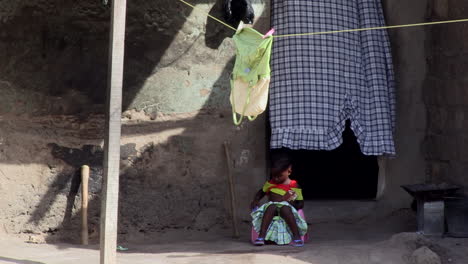 African-child-sitting-in-front-of-the-house-brushes-her-skirt,-door-curtain-flutters-in-the-wind