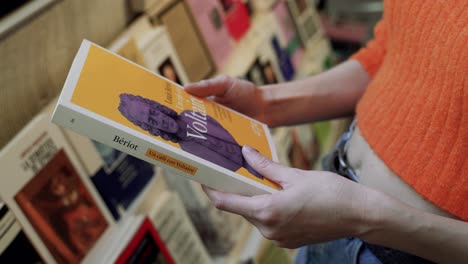 Manos-De-Mujer-Caucásica-Sosteniendo-Un-Libro-De-Literatura-Francesa-En-Una-Librería