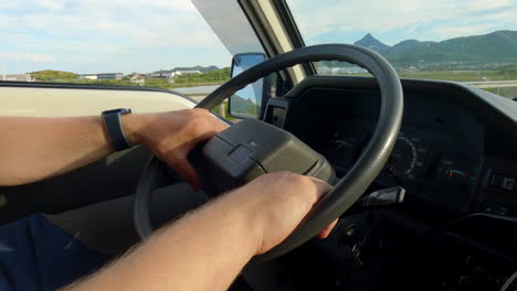 Close-up-shot-of-person-hands-on-the-steering-wheel-while-driving-through-the-countryside-in-a-region-with-few-trees-and-mountains-in-the-distance