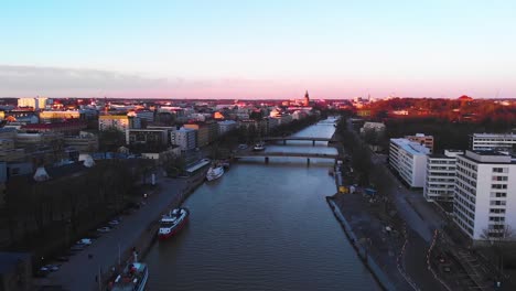 Aerial,-drone-shot-over-the-Aurajoki-river,-overlooking-the-city-of-Turku,-during-sunset,-in-Varsinais-suomi,-Finland