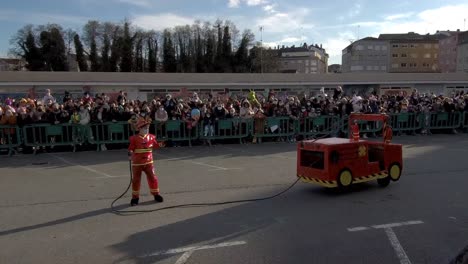 Un-Niño-Disfrazado-De-Bombero-Con-Un-Camión-De-Juguete-Actúa-Para-La-Multitud-En-El-Carnaval-De-Ordes,-España