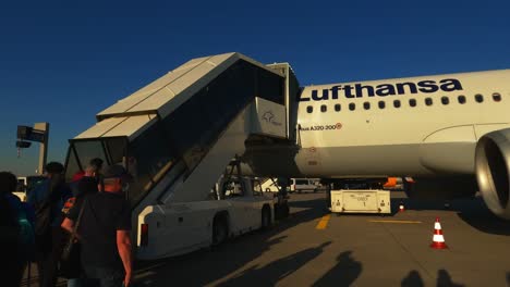 Pasajeros-Subiendo-A-Un-Avión-De-Lufthansa-A-Través-De-Las-Escaleras-Que-Salen-De-La-Pista-En-El-Aeropuerto-Internacional-De-Frankfurt,-Alemania,-Toma-Manual