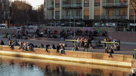 People-hanging-out-during-aperitivo-in-Milan-Italy-on-the-Naviglio-Grande-canal,-slow-panning-wide-shot