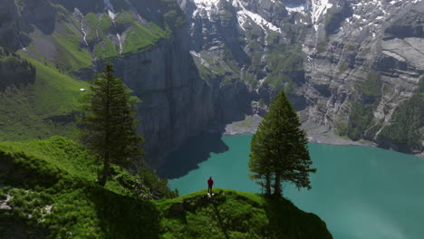 Man-Standing-On-Cliff-Appreciating-The-Beauty-Of-Oeschinen-Lake-In-Switzerland---Aerial-Shot