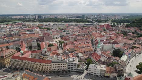 Bratislava's-historic-old-town-with-red-rooftops-and-distant-modern-cityscape,-aerial-view