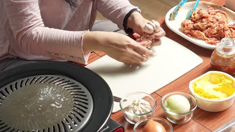 Woman-Peeling-Garlic-By-Hand-On-Cutting-Board-In-Preparation-Making-Asian-Barbeque