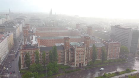 Aerial-view-of-a-notable-red-brick-building-complex-set-against-the-backdrop-of-a-cityscape,-showcasing-its-intricate-architecture-amidst-a-misty-atmosphere-in-Vienna,-Austria