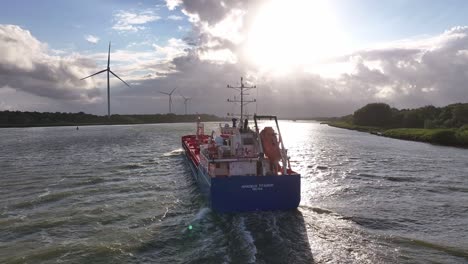 Cargo-ship-navigating-a-river-with-wind-turbines-at-sunset