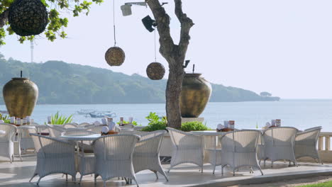 Elegant-beachside-restaurant-with-stylish-seating-and-panoramic-ocean-views-in-Bali,-slow-pan-left-as-lanterns-sway-in-wind