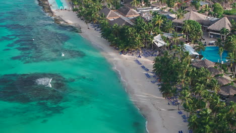 Aerial-shot-of-Bayahibe-beach-at-sunny-morning,-panning-of-coastline,-where-people-enjoys-vacation-on-clear-Caribbean-sea-in-Dominican-Republic