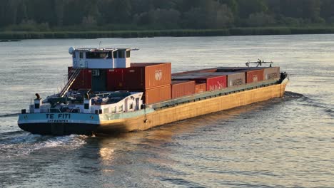 Aerial-drone-reveals-nostalgic-cargo-ship-sailing-with-containers-on-top,-dutch-river-waters,-establishing-panoramic