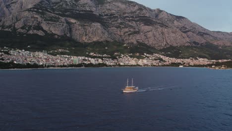 Barco-Turístico-En-La-Costa-De-La-Ciudad-De-Makarska,-Croacia,-Asentado-Bajo-Una-Montaña