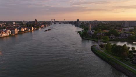 Ein-Ruhiger-Fluss,-Der-Bei-Sonnenuntergang-Durch-Eine-Stadt-Fließt,-Mit-Einer-Brücke-In-Der-Ferne