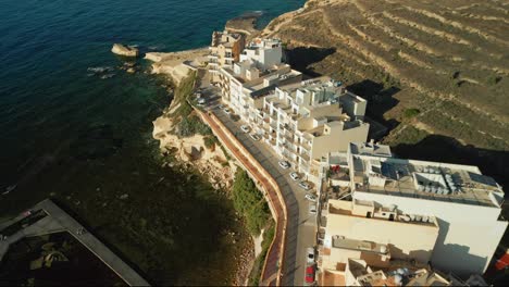 Aerial-footage-revealing-the-coastline-along-the-harbour-of-Marsalforn-during-evening-golden-hour-in-Gozo,-Malta