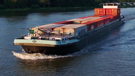 Large-vessel-container-ship-Te-Fiti-sails-at-Dutch-calm-waters-with-flags-waving,-delta-green-fields-background