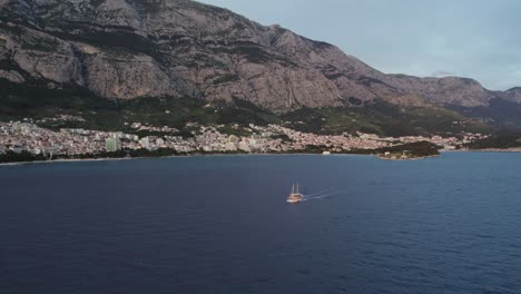 Tourist-boat-in-calm-Adriatic-sea,-Makarska-town-near-mountain,-Croatia