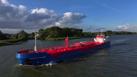 Aerial-view-of-cargo-ship-sailing-on-river-with-lush-green-landscape-under-blue-skies