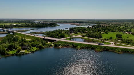 Vehicles-Driving-On-Road-On-The-Banks-Of-Lielupe-River-In-Marupe,-Latvia