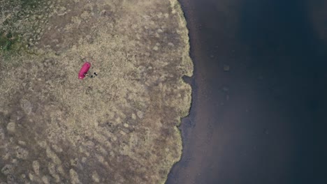 Un-Hombre-Y-Su-Perro-Descansan-Junto-A-Una-Tienda-De-Campaña-Instalada-En-La-Orilla-Del-Lago-Kjøåkertjønna-En-Osen,-Condado-De-Trøndelag,-Noruega:-Toma-Aérea-Desde-Arriba