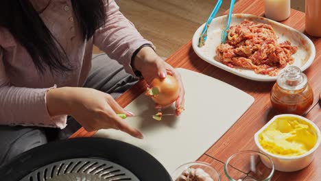 Mujer-Cortando-Cebollas-En-Una-Tabla-De-Cortar-Con-Un-Cuchillo,-Preparándose-Para-Hacer-Una-Barbacoa-Coreana