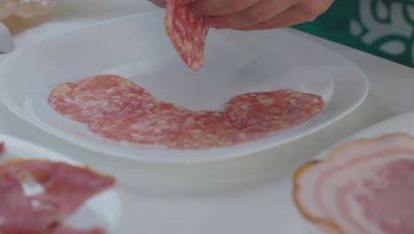 Un-Chef-Colocando-Carnes-Cortadas-En-Rodajas-Sobre-Una-Tabla,-Preparándolas-Para-Una-Presentación-De-Charcutería.