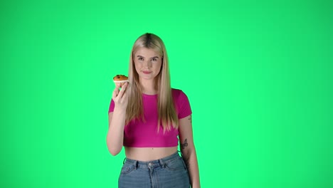 Portrait-Of-Greedy-Young-Blonde-Woman-Smelling-and-Eating-Muffin-Pastry,-Studio-Shot-With-Green-Background