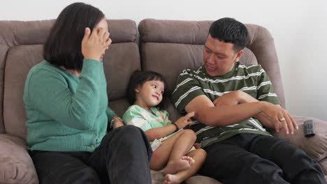 Familia-Asiática-Feliz-Sentada-En-El-Sofá-En-Casa,-Bromeando-Y-Haciéndose-Cosquillas-Unos-A-Otros