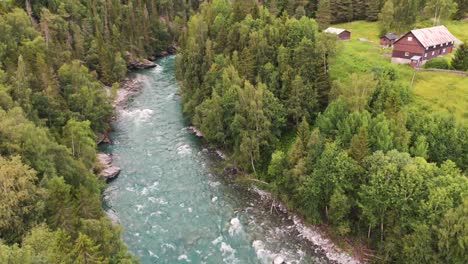 Luftaufnahme-Eines-Gewundenen-Flusses,-Der-Durch-Ein-Dichtes-Bewaldetes-Tal-Mit-üppigen-Grünen-Bäumen-Und-Ein-Paar-Häusern-Im-Hintergrund-Fließt