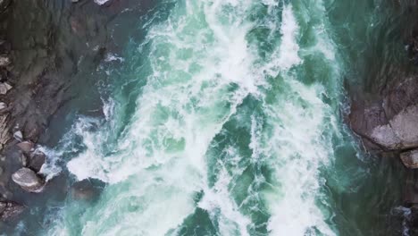 Aerial-stunning-birds-eye-view-of-white-water-rapids-flowing-vigorously-over-rocks,-showcasing-the-power-and-movement-of-nature